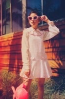 Woman in pink tweed dress adjusting heart-shaped sunglasses with retro styling