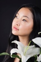 Profile portrait against dark background with long black hair holding white lilies